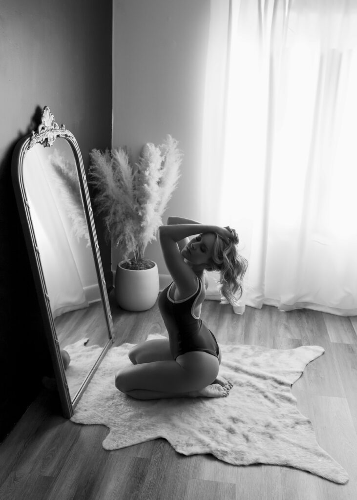 black and white photo of woman kneeling on floor in front of mirror for a boudoir  session. 