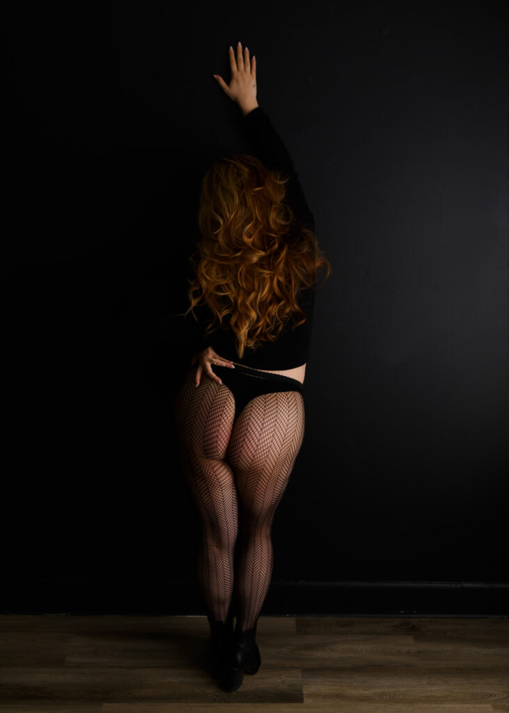 woman in black turtleneck, thong, fishnets and boots posing at a boudoir photoshoot in Richmond Virginia 