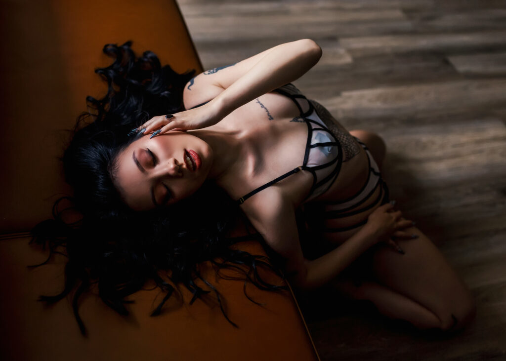 Boudoir client posing on leather sofa in sexy black and nude lingerie. 