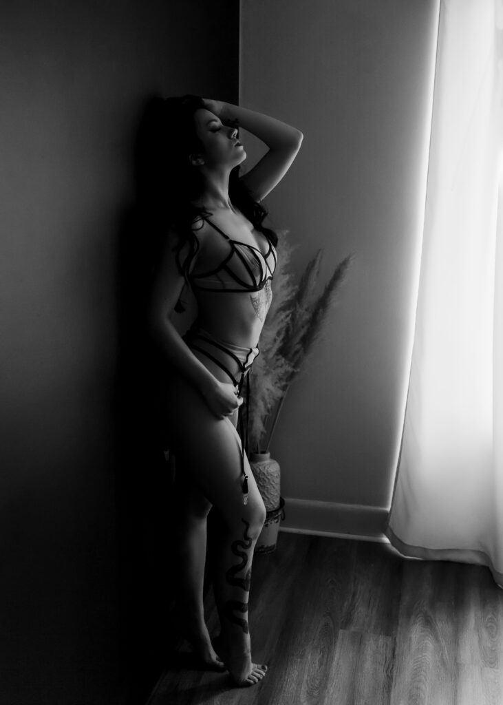 Black and white photo of woman in a sexy boudoir pose leaning against  wall. 
