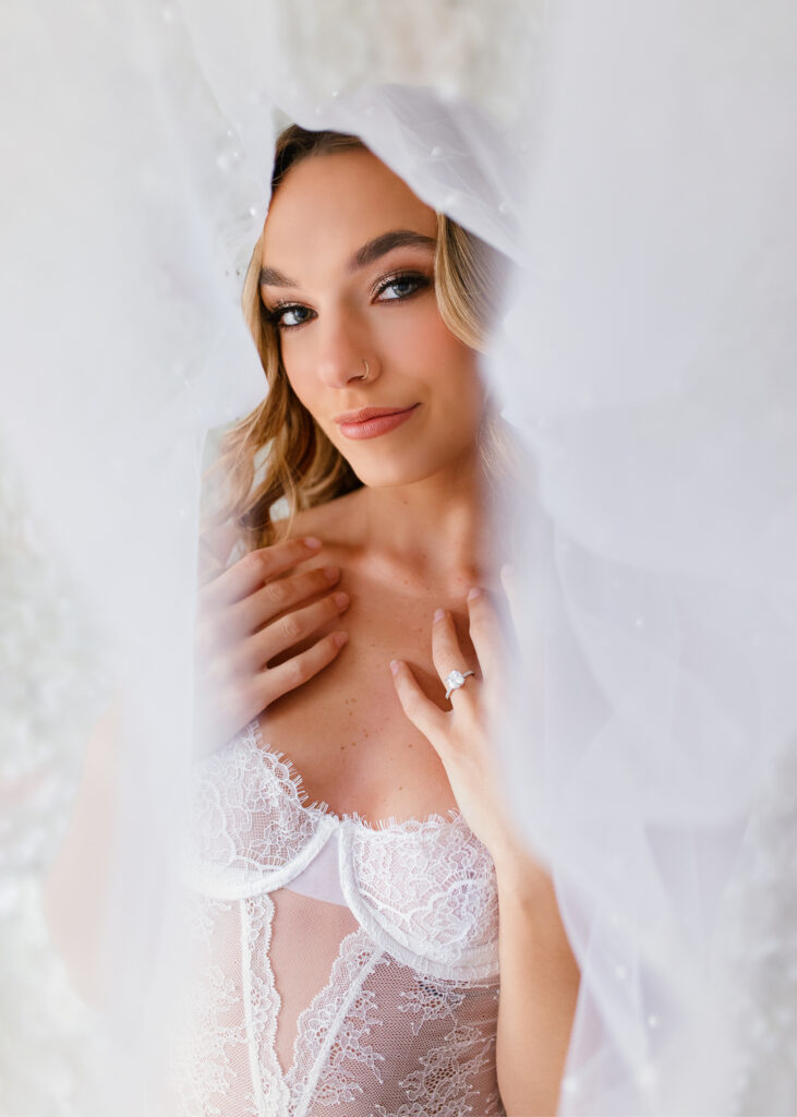 bride is posing with white lingerie, wedding veil, and engagement ring during a bridal boudoir photoshoot in Richmond Virginia 