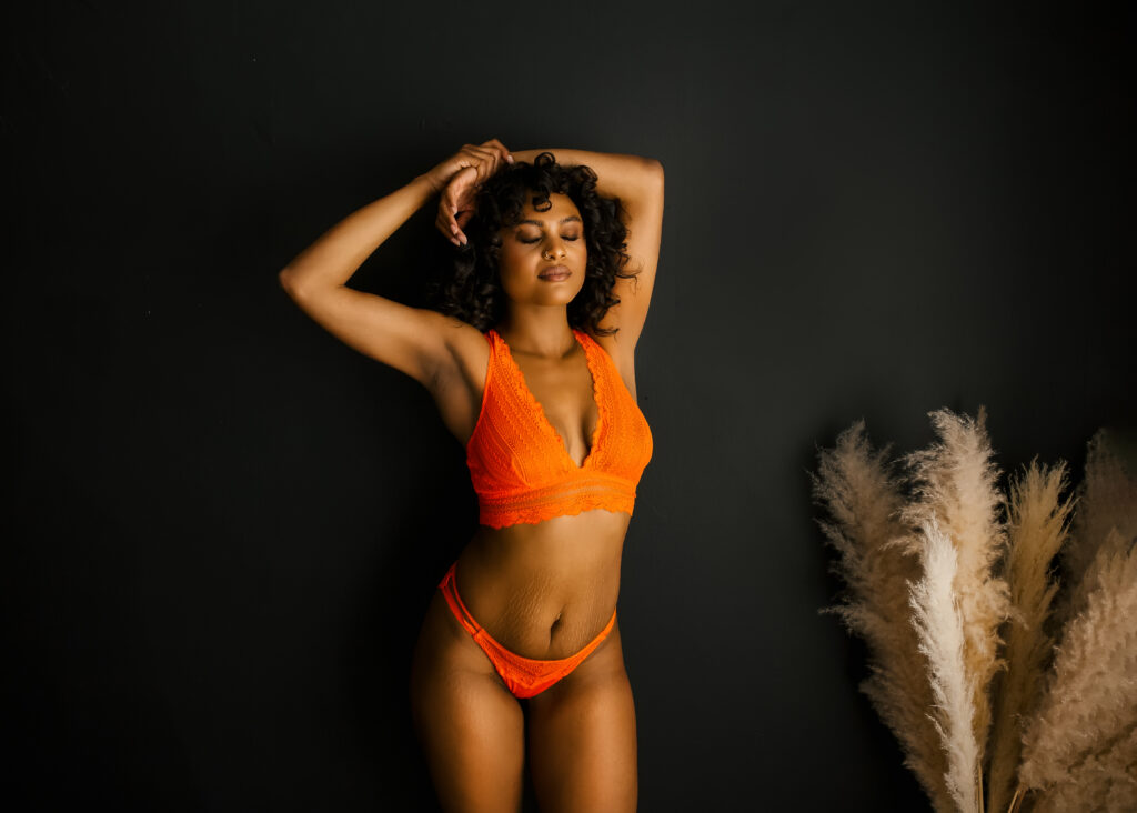 Beautiful black woman posing on wall in orange lace bra and panty during a boudoir photoshoot in Richmond Virginia