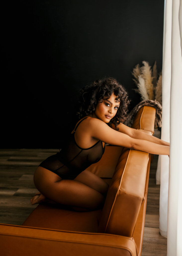 Beautiful black woman posing in mesh lingerie on back of couch during a boudoir photoshoot in Richmond Virginia. 