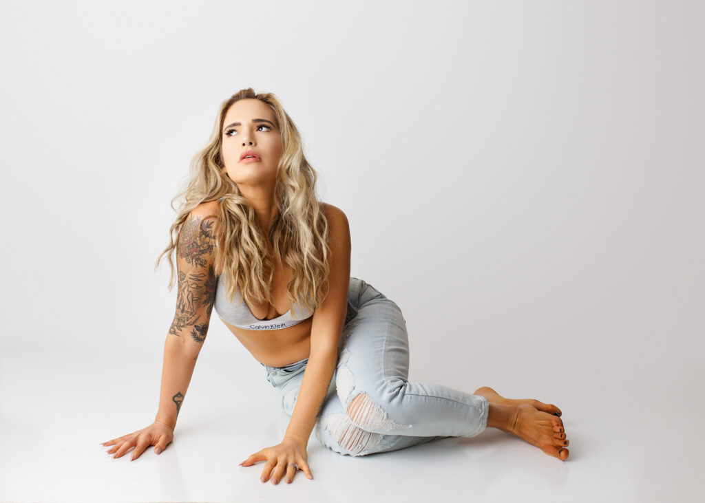 Woman posing  on white backdrop in barrette and ripped jeans simple outfit for a boudoir photo shoot. 