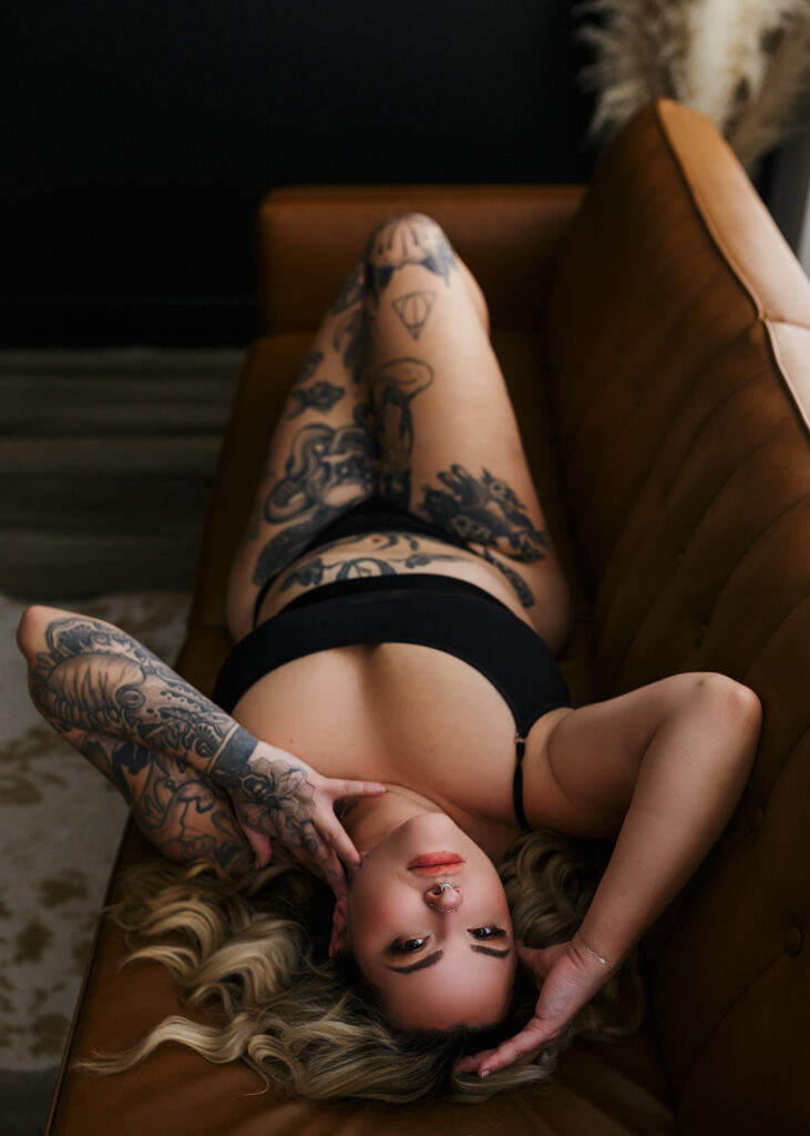 Tattooed woman posing on leather sofa posing for a boudoir  photographer in Richmond, VA. 
