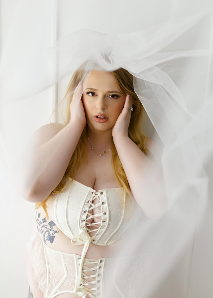 plus size woman posing in white bridal lingerie and wedding viel for a bridal boudoir photo shoot in richmond Virginia 